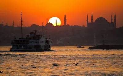 Una barca da crociera in legno che naviga sul Bosforo con lo skyline illuminato dal tramonto